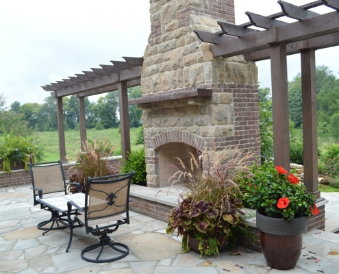 An outdoor stone fireplace with an attached pergola