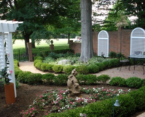 A garden surrounding a brick walkway with flowers and a statue.