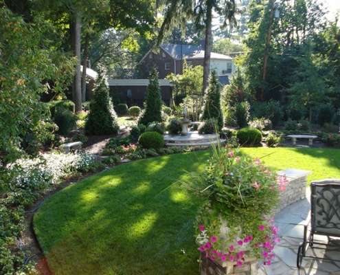 A landscape with a large garden, patio, flower pot accents, and stone features in Louisville, Kentucky