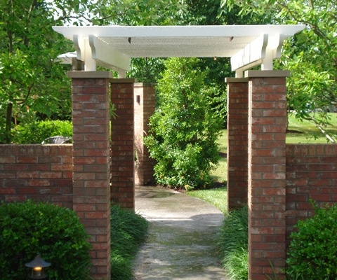 A landscape structure made with a white pergola and brick pillars attached to brick walls.