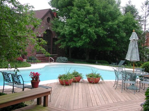 A swimming pool with accent pots on a wooden deck surrounded by landscape features
