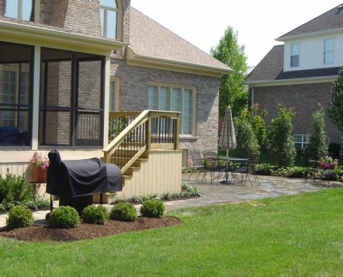 A woodwork deck with stairs leading to a stone patio